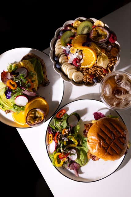 Gedeckter Tisch mit Frühstücksburger, Açaí-Bowl und Cold Brew